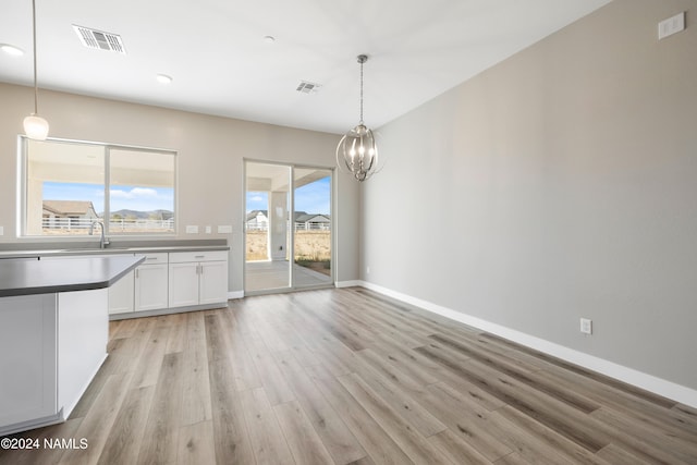 unfurnished dining area with sink, an inviting chandelier, and light wood-type flooring