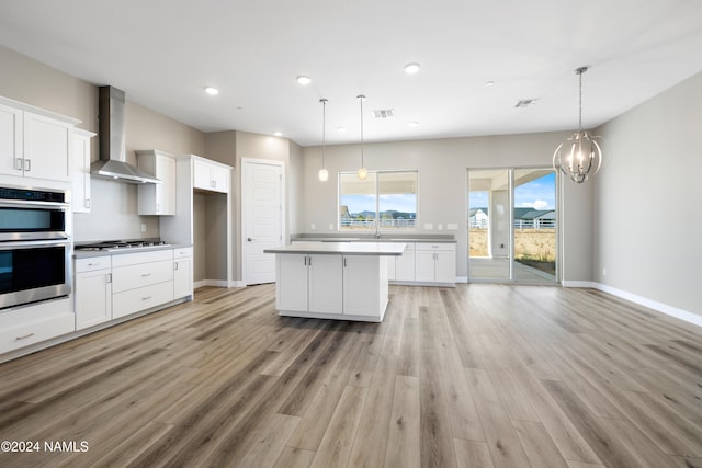 kitchen featuring white cabinets, a kitchen island, pendant lighting, stainless steel appliances, and wall chimney exhaust hood