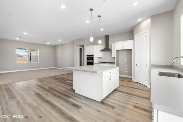 kitchen with a center island, hanging light fixtures, sink, wall chimney range hood, and white cabinets