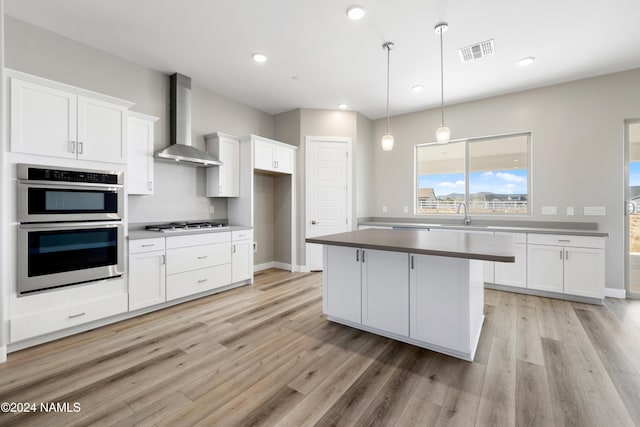 kitchen with wall chimney range hood, white cabinets, light hardwood / wood-style flooring, and hanging light fixtures