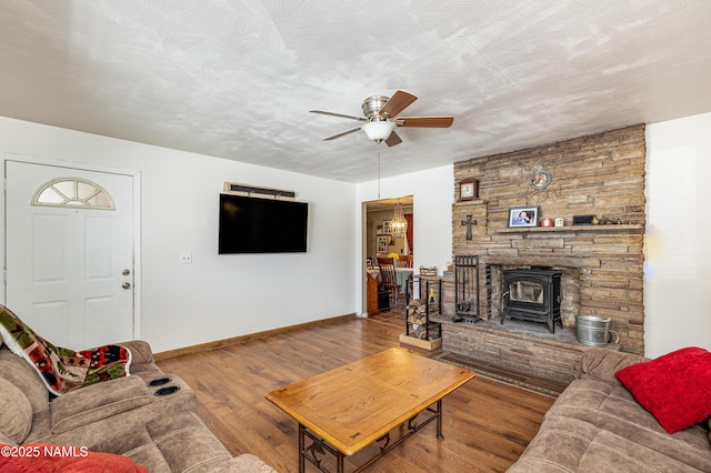 living room with a textured ceiling, wood finished floors, baseboards, ceiling fan, and a wood stove