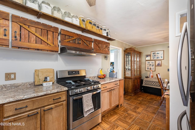 kitchen featuring refrigerator, light stone countertops, gas stove, and under cabinet range hood