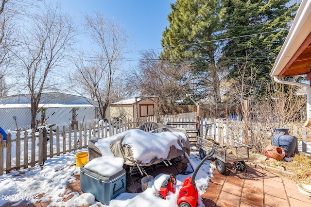 yard layered in snow featuring an outdoor structure, outdoor dining area, fence, and a storage unit