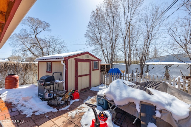 snow covered structure with an outbuilding, a storage unit, and a fenced backyard