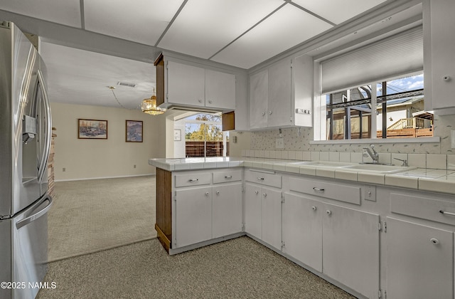 kitchen with visible vents, light carpet, a sink, a peninsula, and stainless steel fridge