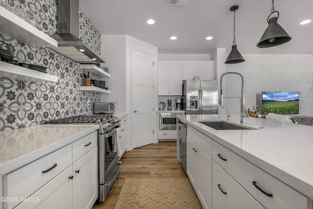 kitchen featuring open shelves, wall chimney range hood, decorative light fixtures, stainless steel appliances, and a sink