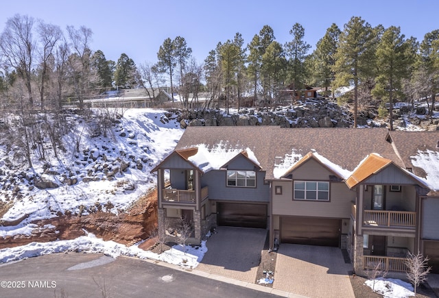 rustic home featuring a balcony, stone siding, a garage, and driveway