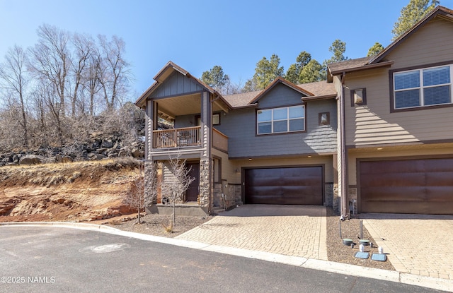 view of front facade with stone siding, a balcony, decorative driveway, and a garage