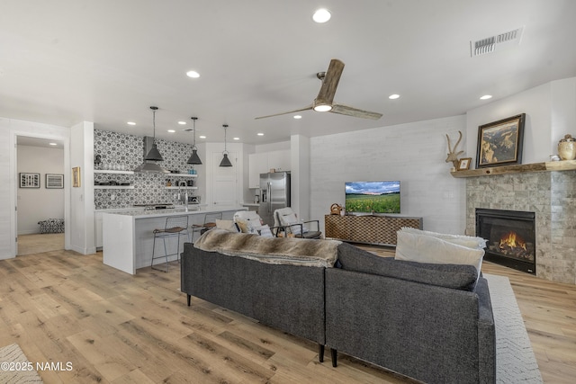 living room featuring light wood finished floors, visible vents, recessed lighting, a fireplace, and a ceiling fan