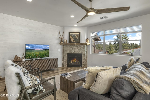 living area featuring ceiling fan, visible vents, wood finished floors, and a tile fireplace