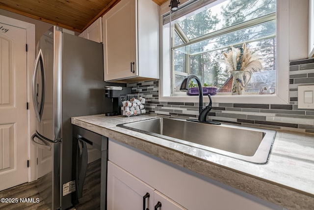 kitchen featuring a sink, backsplash, black dishwasher, freestanding refrigerator, and white cabinets