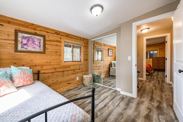 bedroom featuring lofted ceiling, wood finished floors, a closet, wooden walls, and baseboards