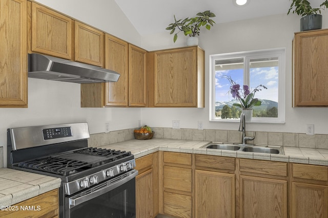 kitchen with tile countertops, lofted ceiling, a sink, under cabinet range hood, and stainless steel gas stove