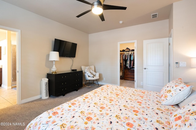 bedroom with light colored carpet, a closet, ceiling fan, and a walk in closet