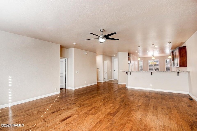 unfurnished living room featuring hardwood / wood-style flooring, ceiling fan, and a textured ceiling