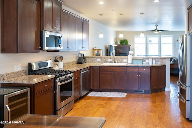 kitchen with pendant lighting, stainless steel appliances, sink, kitchen peninsula, and light stone counters