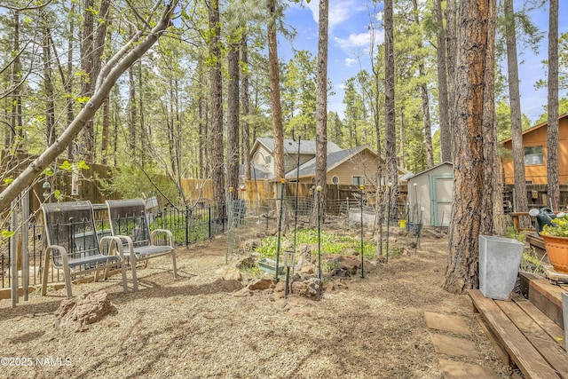 view of yard featuring an outdoor structure, fence, a storage shed, and a vegetable garden