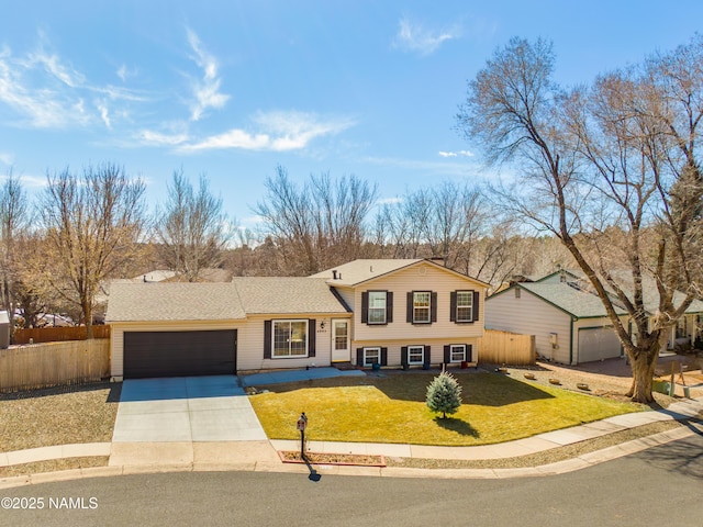 tri-level home featuring a shingled roof, concrete driveway, an attached garage, fence, and a front lawn