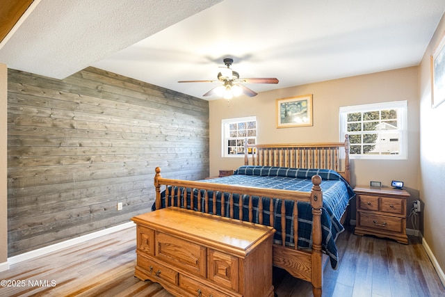 bedroom with light wood-type flooring, wood walls, ceiling fan, and baseboards