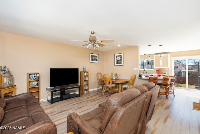 living area with light wood finished floors, a ceiling fan, and baseboards