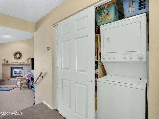 washroom featuring stacked washer / drying machine, a brick fireplace, carpet flooring, and a textured ceiling