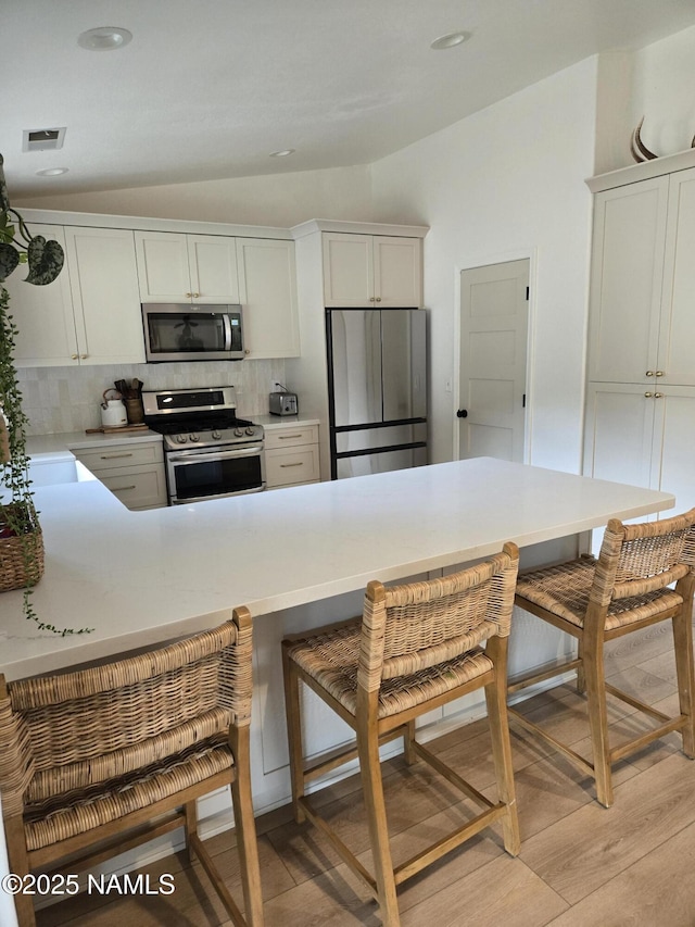 9654 Heritage Dr, Flagstaff, AZ 86004 - kitchen with stainless steel appliances, vaulted ceiling, light wood-style flooring, tasteful backsplash, and a breakfast bar area
