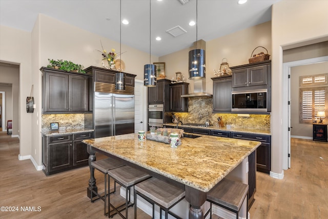 kitchen with a kitchen bar, pendant lighting, a kitchen island with sink, and built in appliances