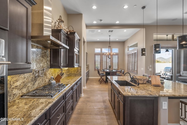 kitchen featuring stainless steel gas stovetop, light stone countertops, a breakfast bar, an island with sink, and wall chimney exhaust hood