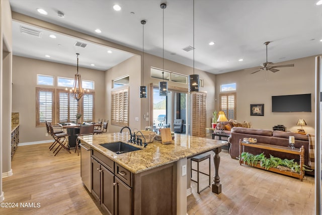 kitchen featuring light stone countertops, decorative light fixtures, an island with sink, sink, and light hardwood / wood-style flooring