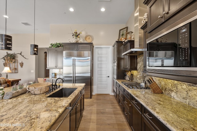 kitchen featuring dark brown cabinets, pendant lighting, sink, light stone countertops, and built in appliances