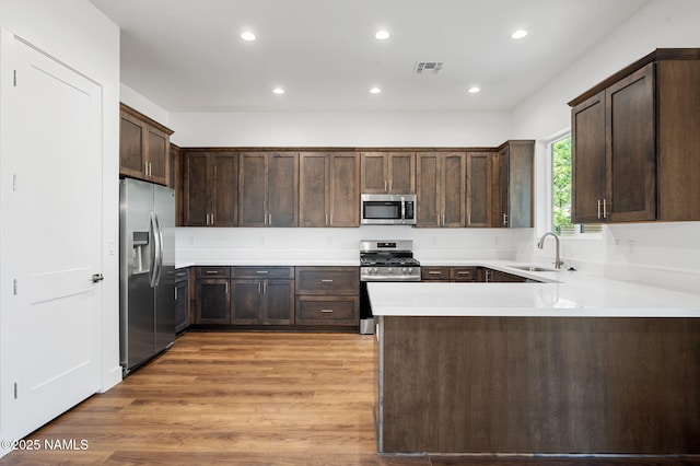 555 N Valerian Ln Lot 24, Flagstaff, AZ 86004 - kitchen with stainless steel appliances, a sink, a peninsula, dark brown cabinetry, and light wood-style flooring