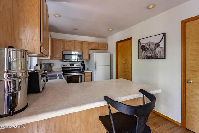 kitchen featuring kitchen peninsula, light hardwood / wood-style floors, a breakfast bar area, and appliances with stainless steel finishes