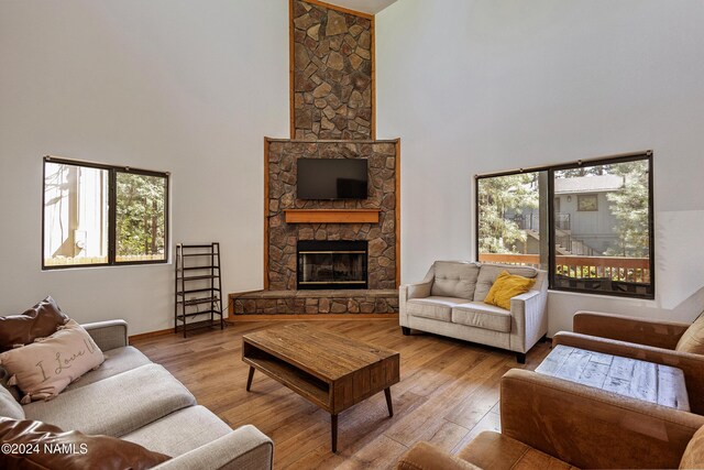 living room featuring a stone fireplace, a high ceiling, and light hardwood / wood-style flooring