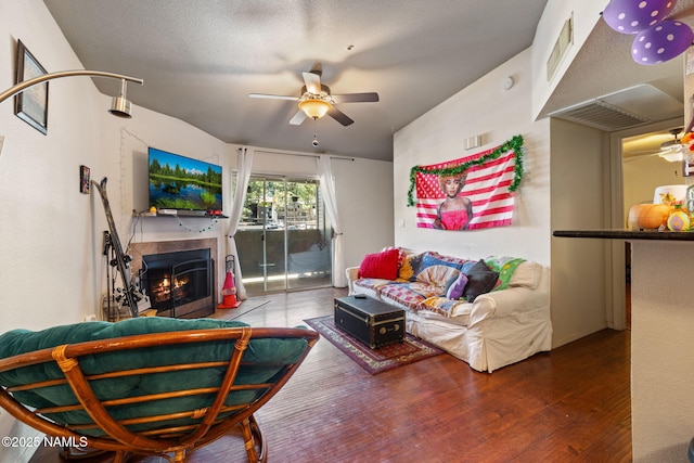 living room with a ceiling fan, a warm lit fireplace, visible vents, and wood finished floors