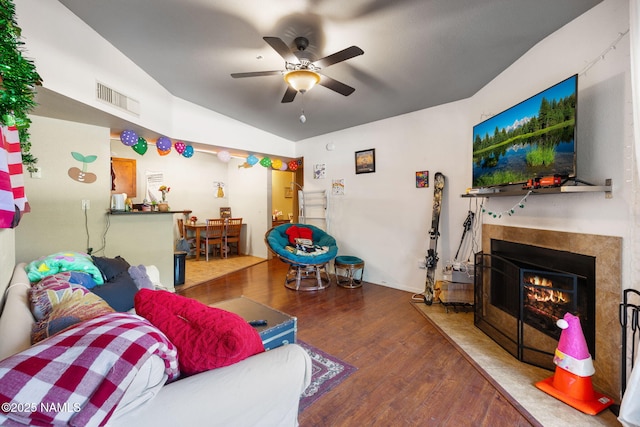 living area with ceiling fan, visible vents, vaulted ceiling, wood finished floors, and a premium fireplace