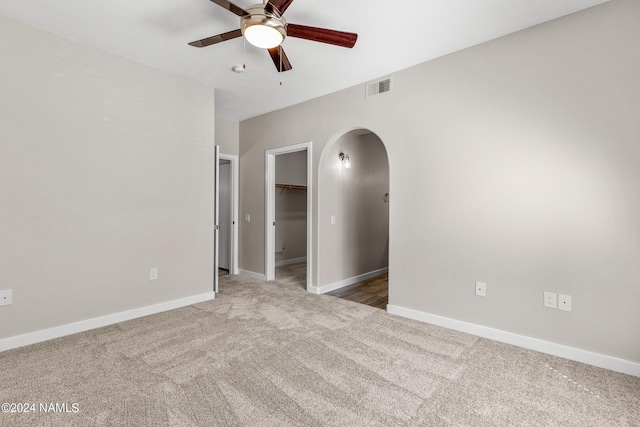 carpeted spare room featuring arched walkways, baseboards, visible vents, and a ceiling fan