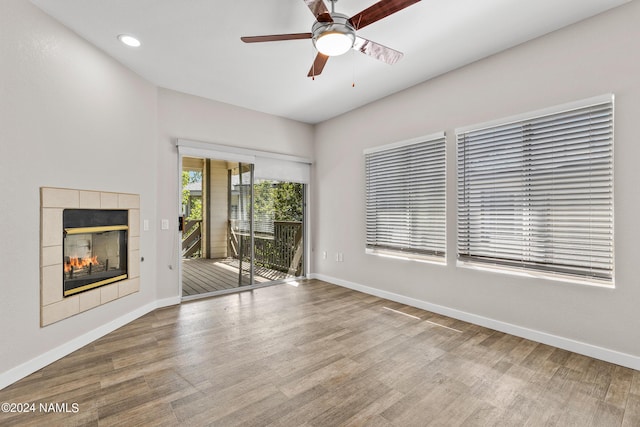 unfurnished living room with a tile fireplace, wood finished floors, a ceiling fan, and baseboards