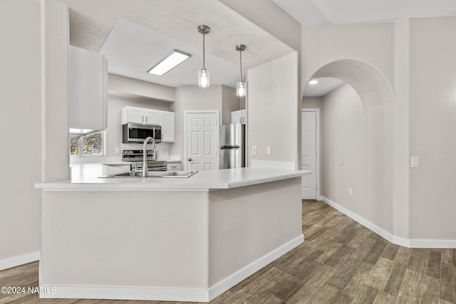 kitchen featuring arched walkways, stainless steel appliances, a peninsula, a sink, and wood finished floors