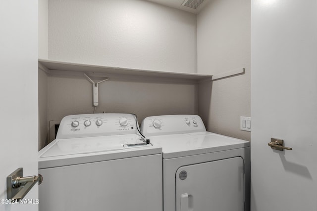 clothes washing area with visible vents, separate washer and dryer, and a textured wall