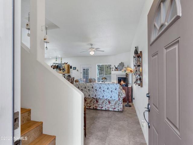 foyer featuring ceiling fan, stairway, a glass covered fireplace, and light tile patterned flooring