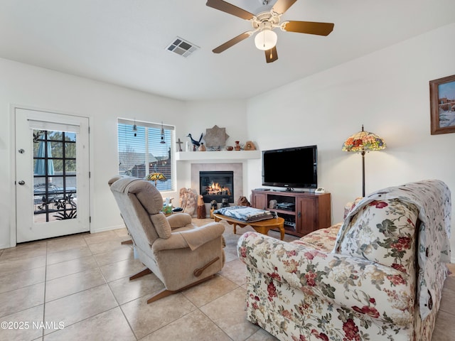 living area with a glass covered fireplace, light tile patterned floors, visible vents, and ceiling fan