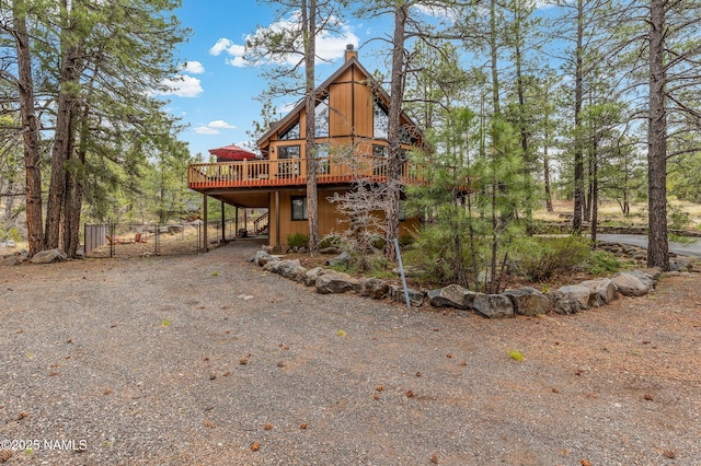 rear view of property with a wooden deck, dirt driveway, a carport, fence, and a chimney