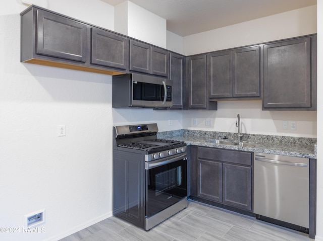 kitchen featuring appliances with stainless steel finishes, dark stone countertops, a sink, and dark brown cabinetry