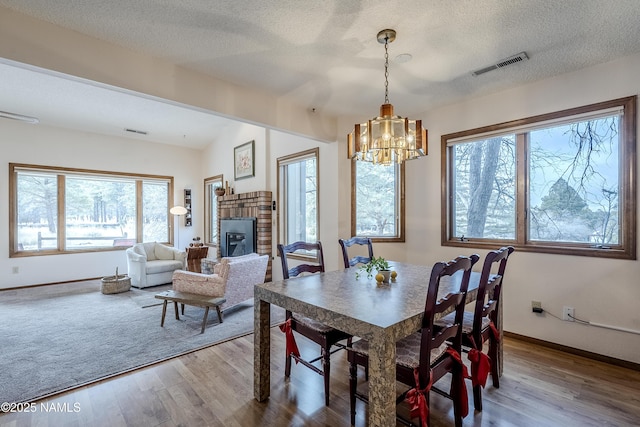 dining area with hardwood / wood-style flooring, a chandelier, a brick fireplace, and a textured ceiling