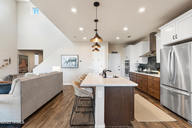 kitchen featuring white cabinetry, a kitchen island with sink, sink, stainless steel appliances, and wall chimney exhaust hood