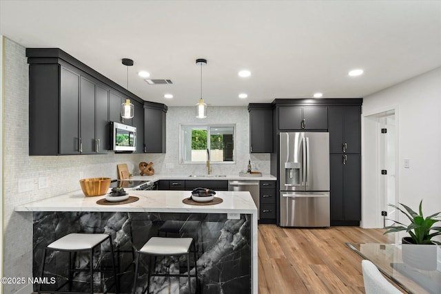 3707 E Amelia Ave, Phoenix, AZ 85018 - kitchen featuring stainless steel appliances, a peninsula, light stone counters, decorative backsplash, and hanging light fixtures