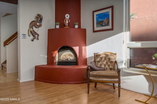 sitting room with a fireplace with raised hearth, stairway, wood finished floors, and baseboards