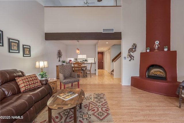 living room featuring light wood-type flooring, a warm lit fireplace, visible vents, and a high ceiling