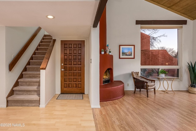 foyer entrance with a lit fireplace, stairway, vaulted ceiling, and wood finished floors