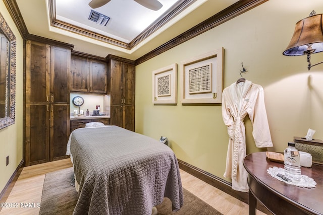 bedroom with light wood-type flooring, a tray ceiling, ceiling fan, and ornamental molding